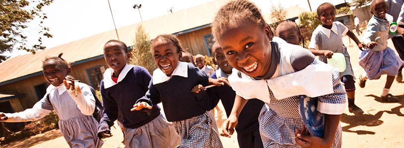 A group of young Kenyan school girls run and laugh at recess.