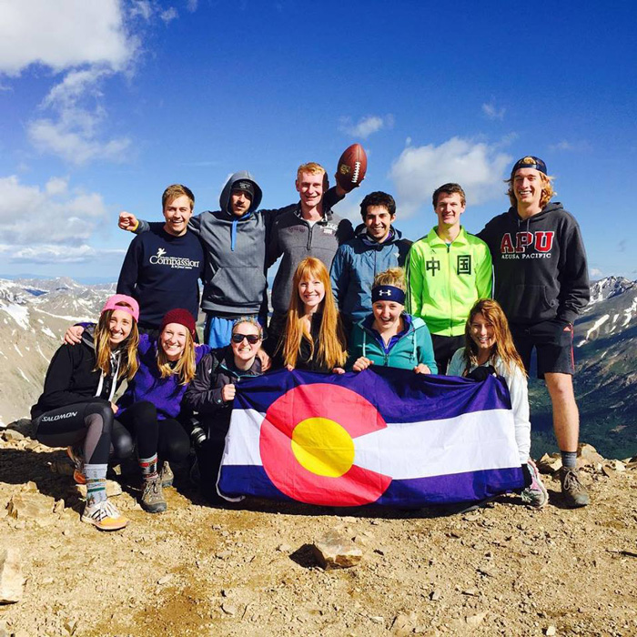 A group of interns holding a Colorado state flag on a mountain top