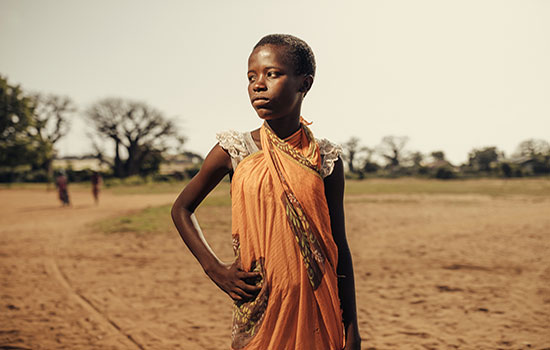 A poor African girl with a serious and dignified expression stands with a hand on her hip