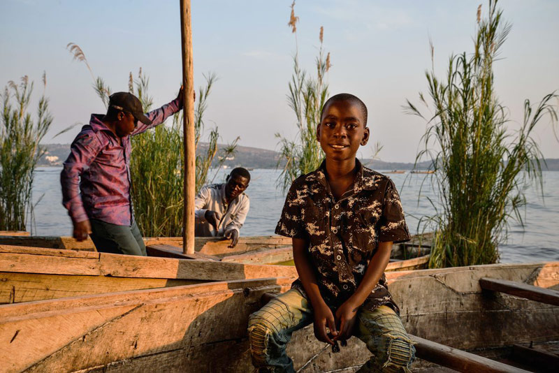 A boy sits near water next to a boat