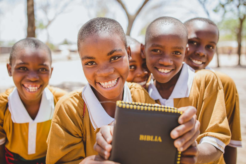 Kids smile holding up a Bible