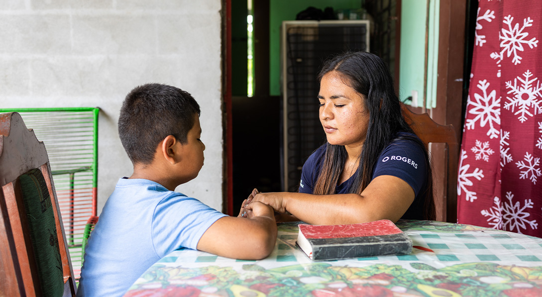 A mom and her son sit together at a table, holding hands while praying.