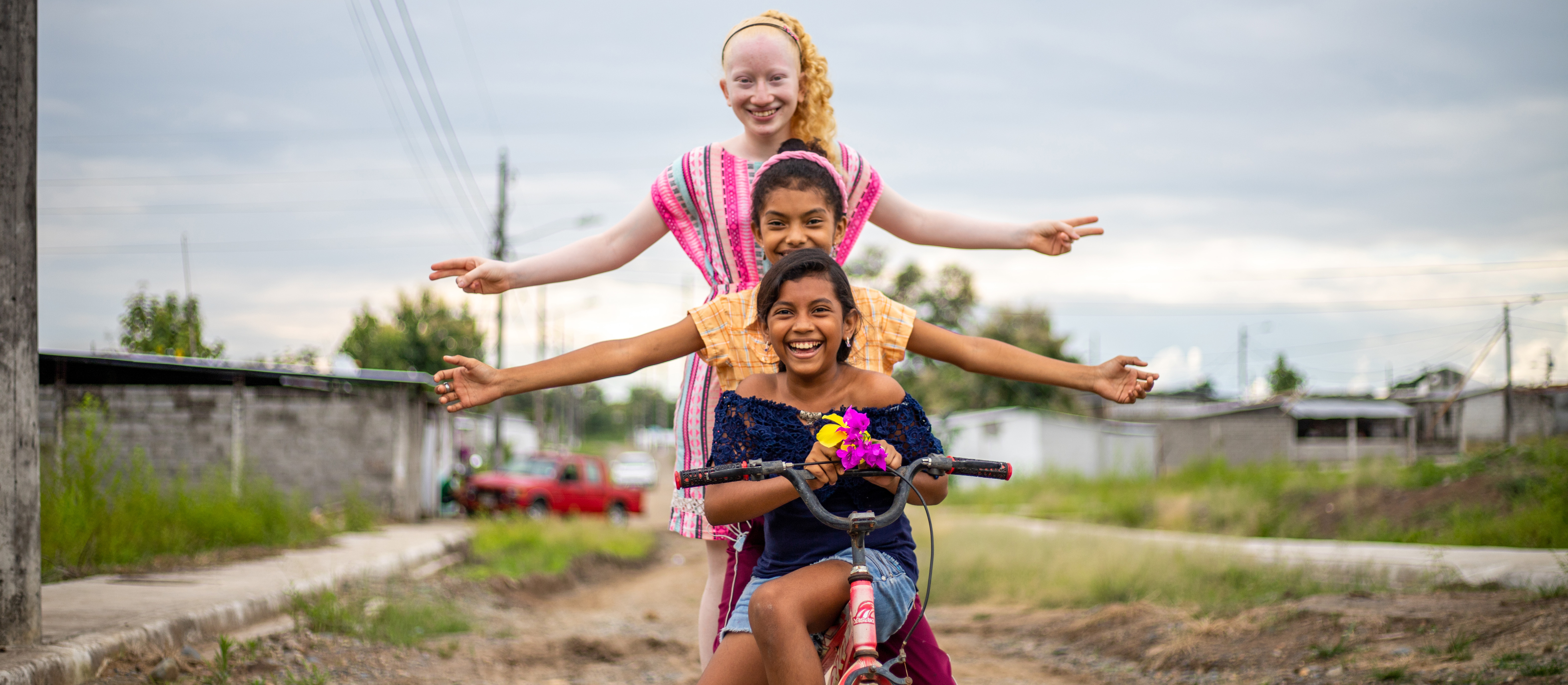 Three girls sit on a bike. Two stretch their arms out while all three smile for the camera.