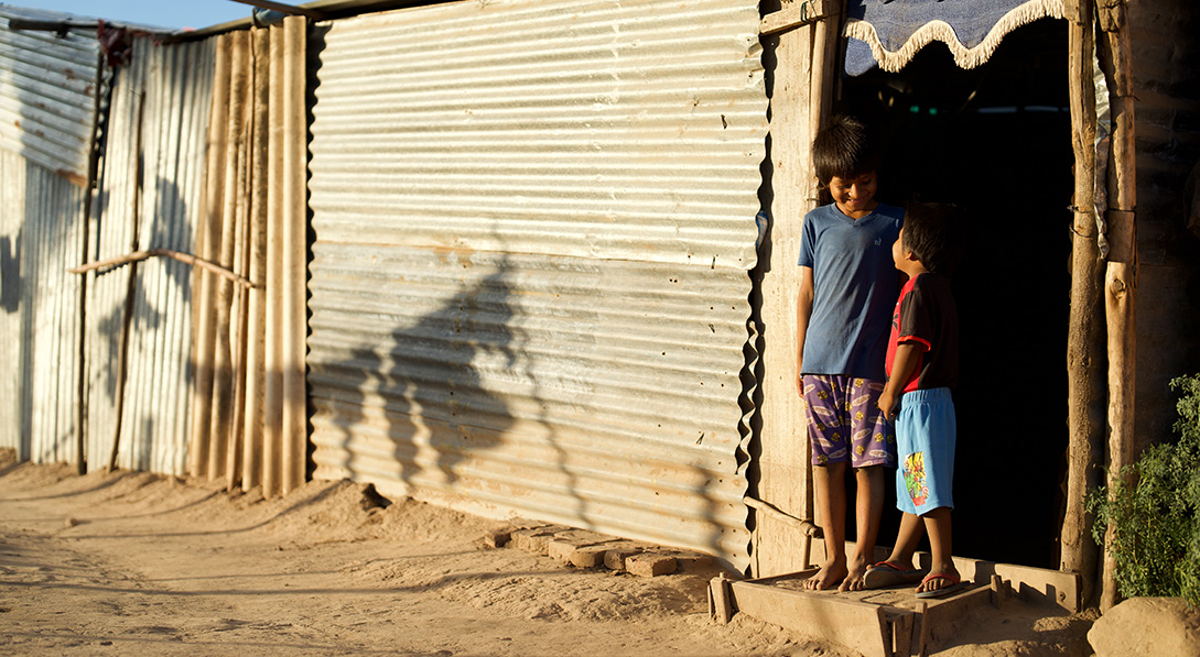 Two young boys stand in a doorway and smile at each other.