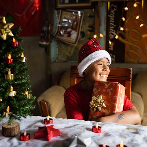 child in santa hat holds gift and smiles