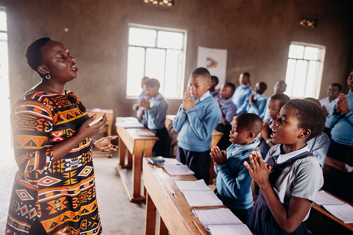 Woman in orange patterend dress leads children in prayer