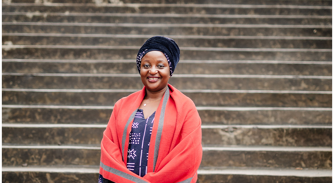 woman in coral jacket stands in front of stairs and smiles