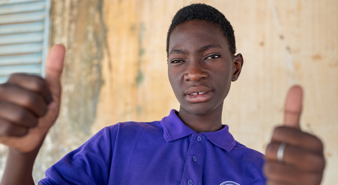 boy in purple shirt puts his thumbs up and looks at the camera