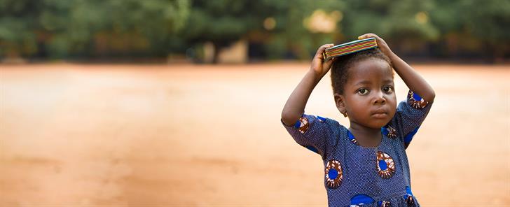 A little girl carrying items on her head.