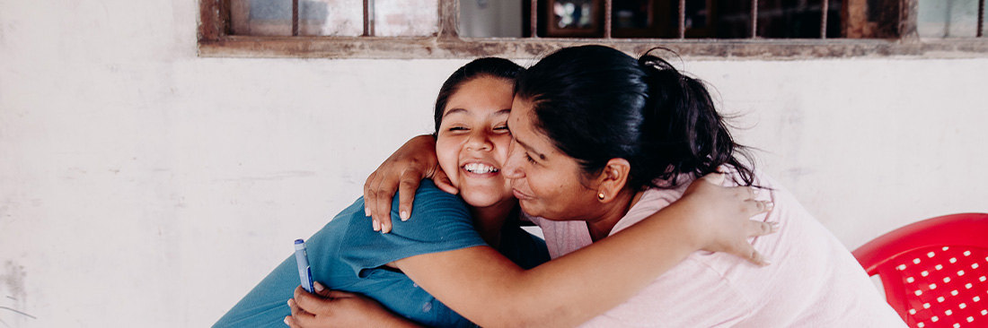 A young girl and her mother hug while sitting in font of a window.