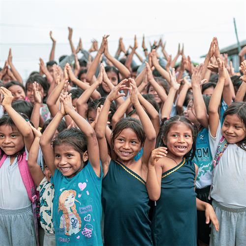 A group of children hold their arms above their heads and smile.