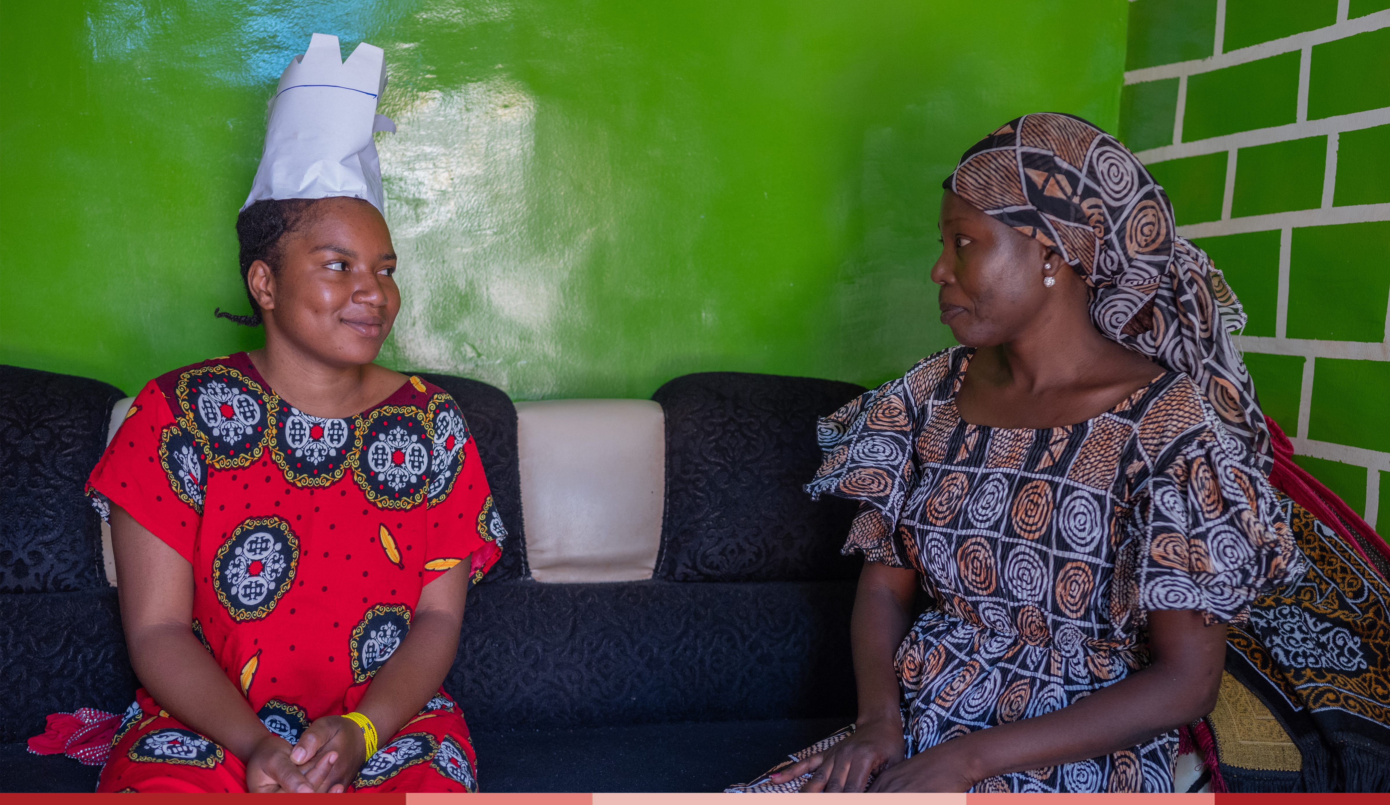 two women sit together in a green living room 