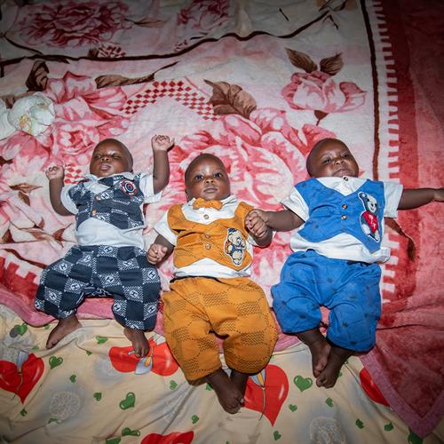 triplets laying down on a quilt in brightly colored onesies