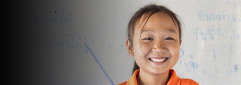  a girl in orange shirt stands in front of white board and smiles