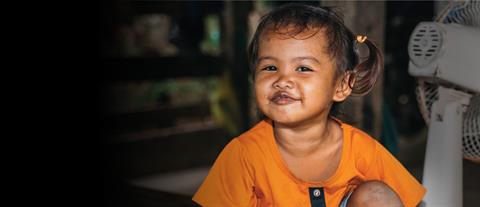 A little girl in an orange t-shirt sits on the floor and smiles