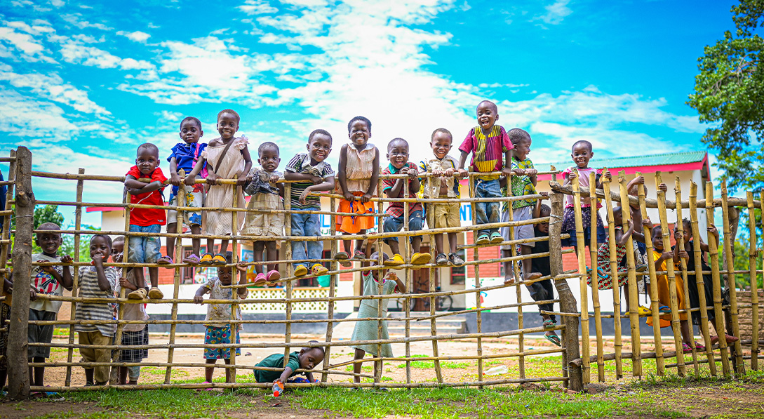 Children stand on fence surrounded by blue sky