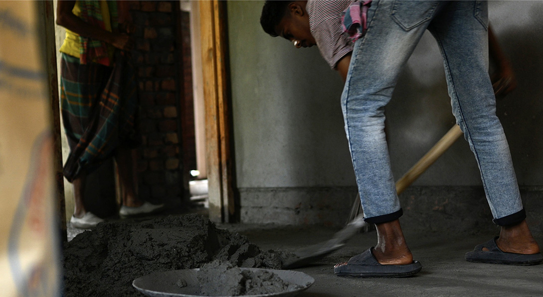 A young boy shovels mortar inside a dark building.