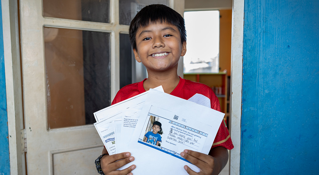 A young boy smiles while proudly showing letters from his sponsor.