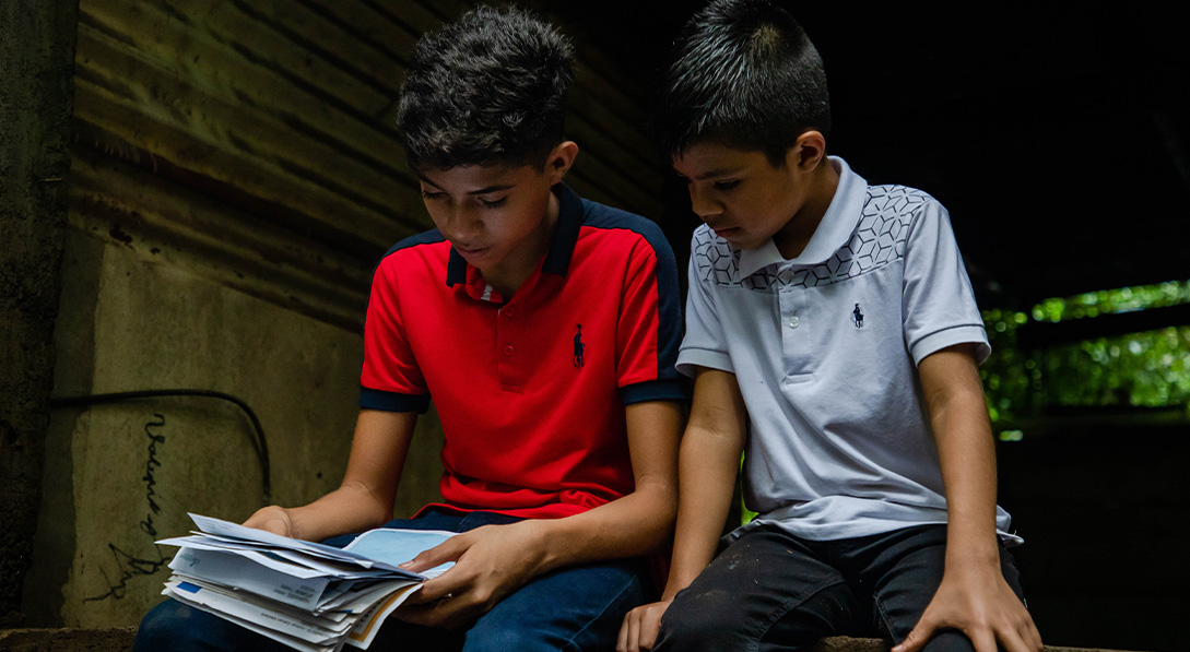 Two boys sit together and read letters from their sponsor.