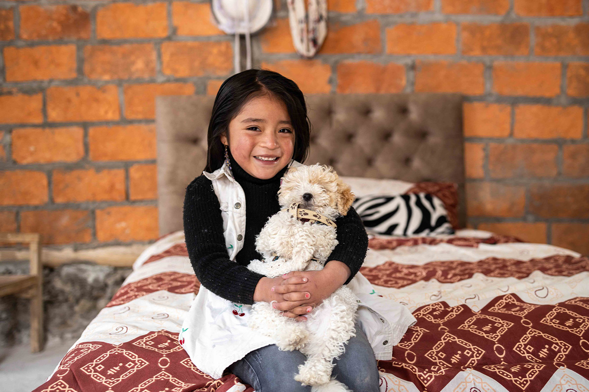 Young girl sits on her bed holding a cute white puppy in her arms.