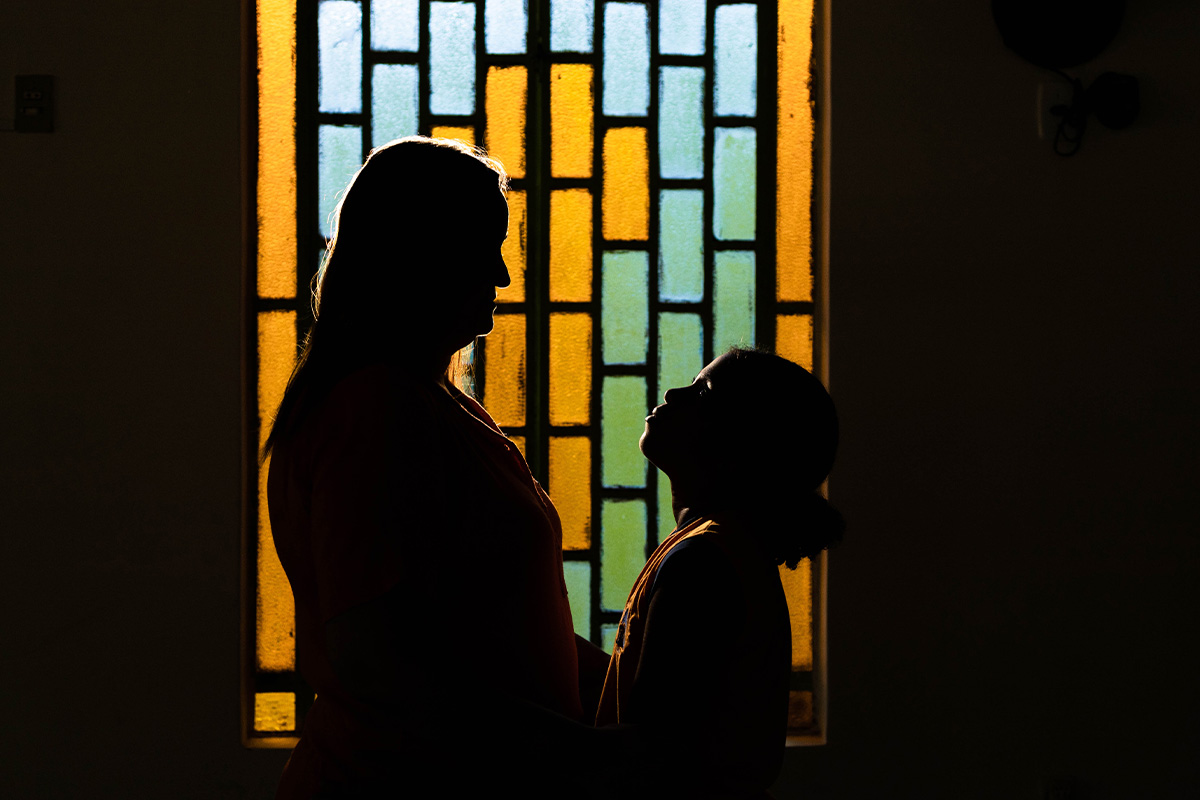 A silhouette of a child protection officer and a child in front of a stained glass window.