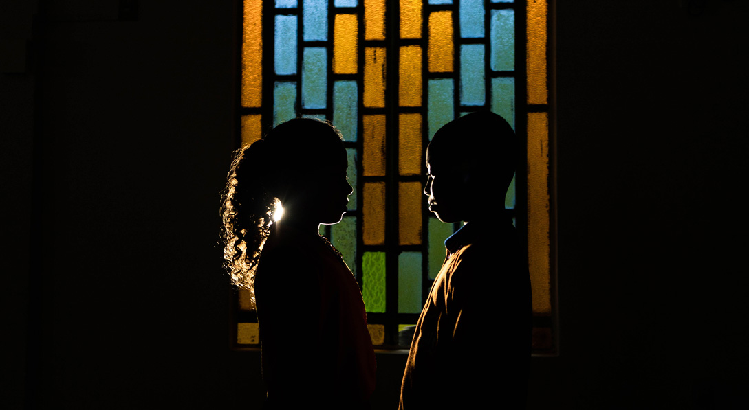 A silhouette of two children in front of a stained glass window.