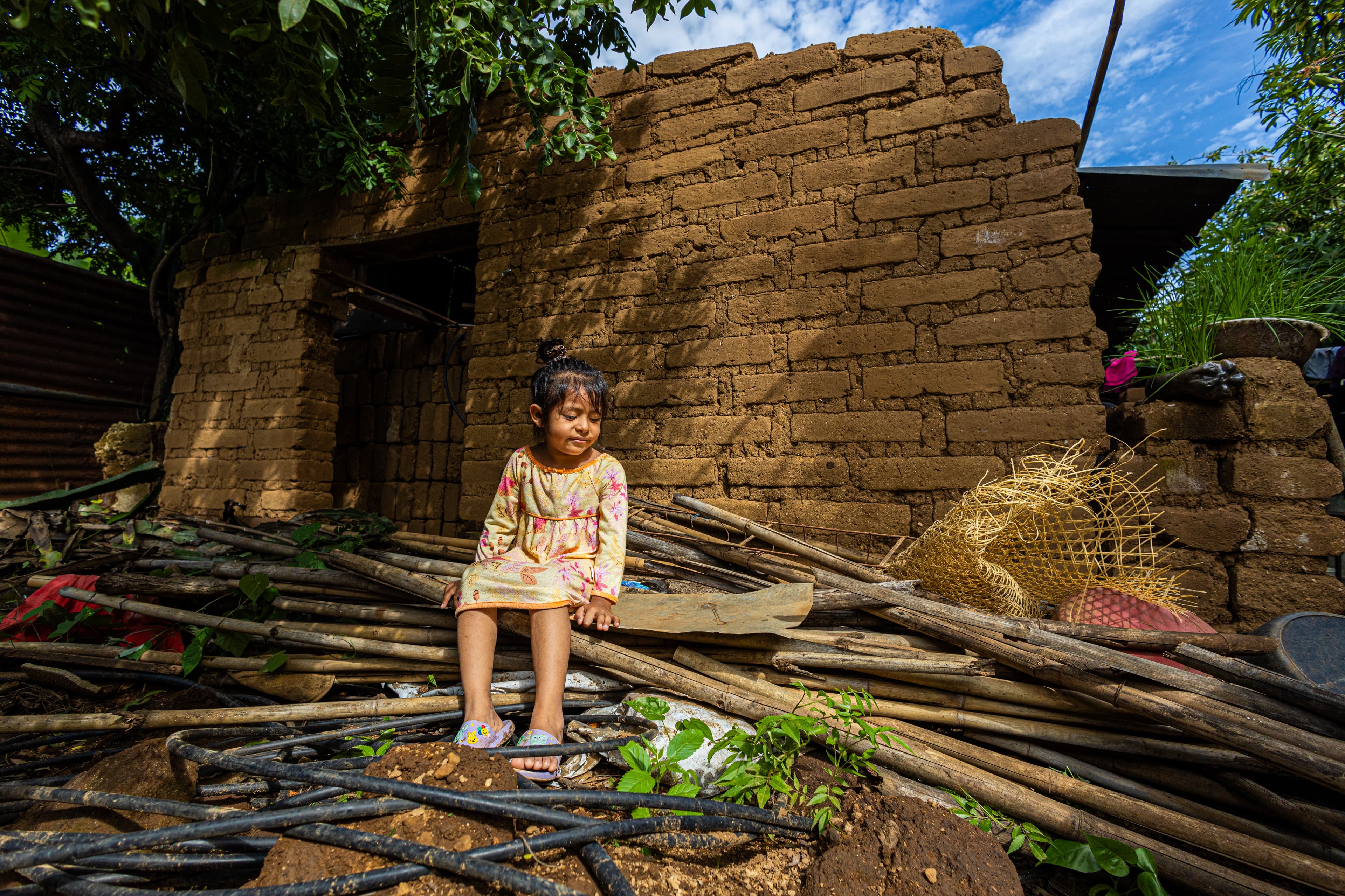 A young girl sits in the rubble of her old house.