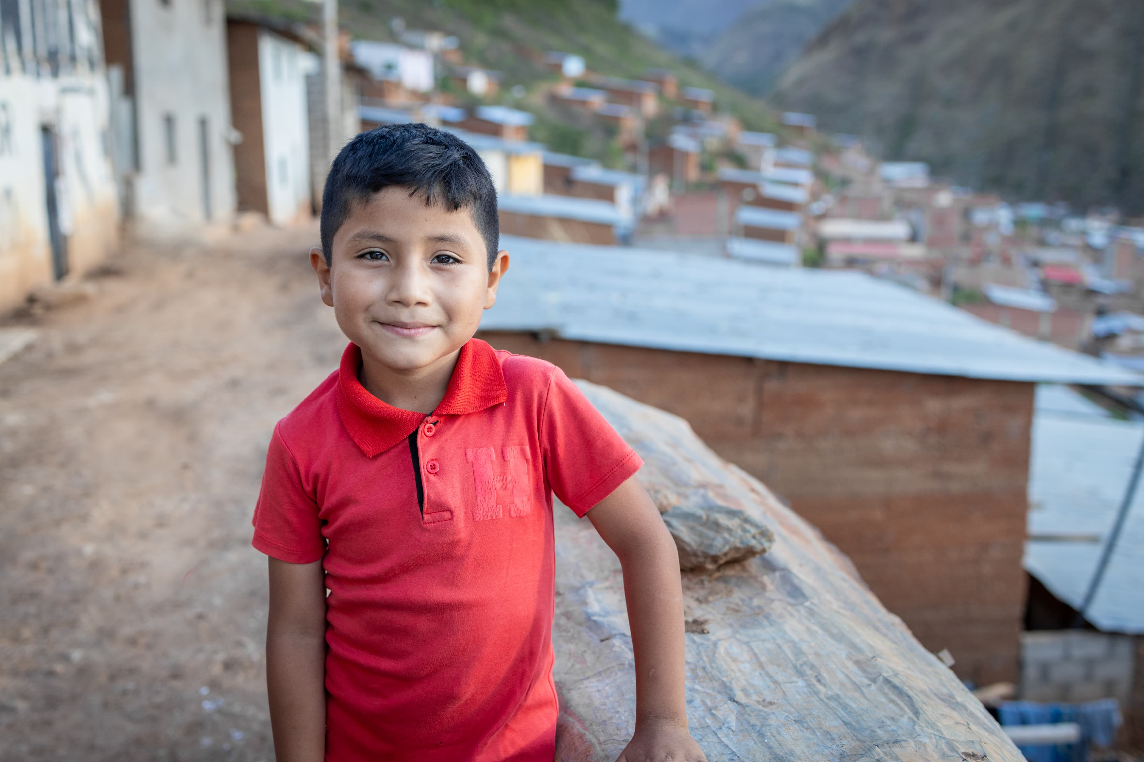 Young boy standing outside his home wearing a red shirt.