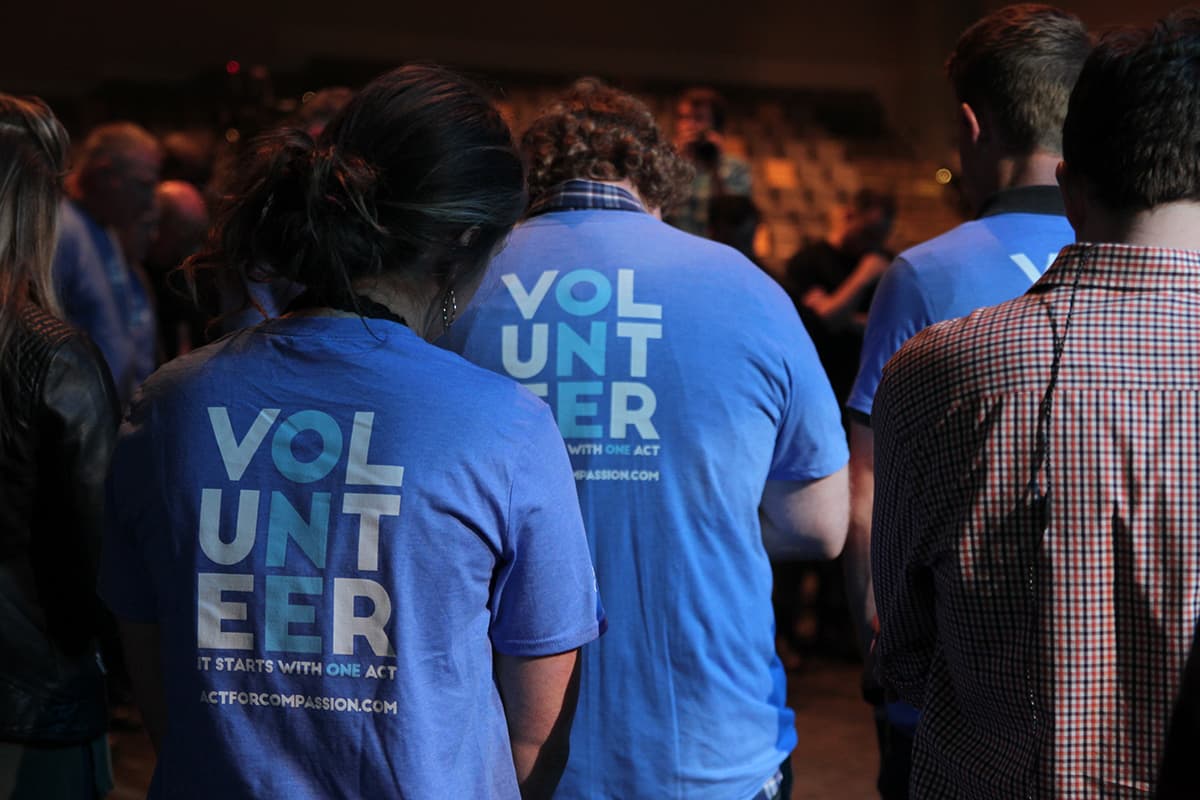 A few people are standing at an event wearing Compassion Volunteer shirts.