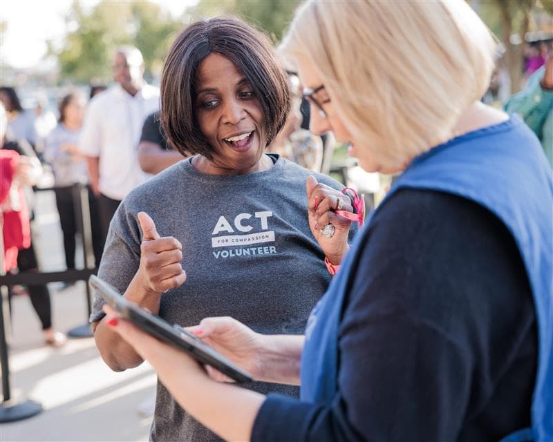 An older woman gives a double thumbs up to another woman.