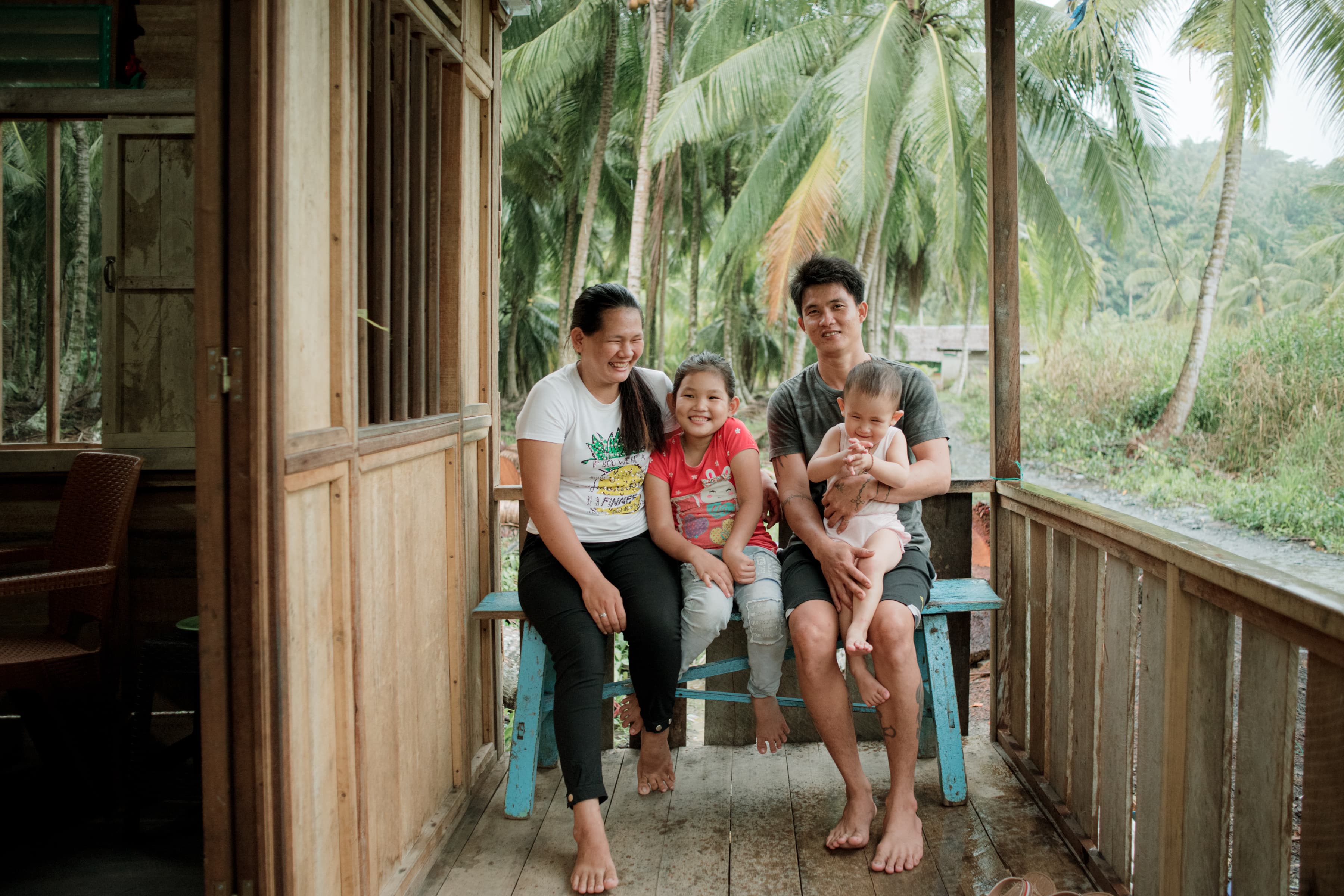 A mother and father sit on a bench holding their two children close while smiling.