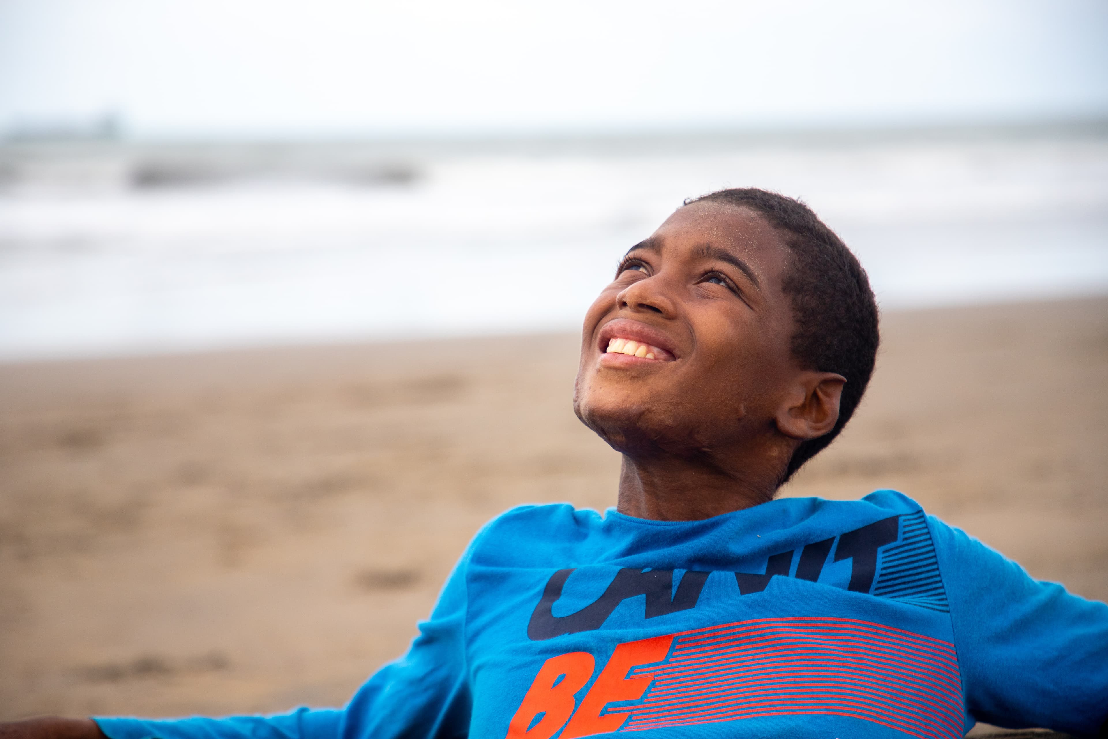 A teen boy wearing a blue shirt looks up to the sky while smiling.