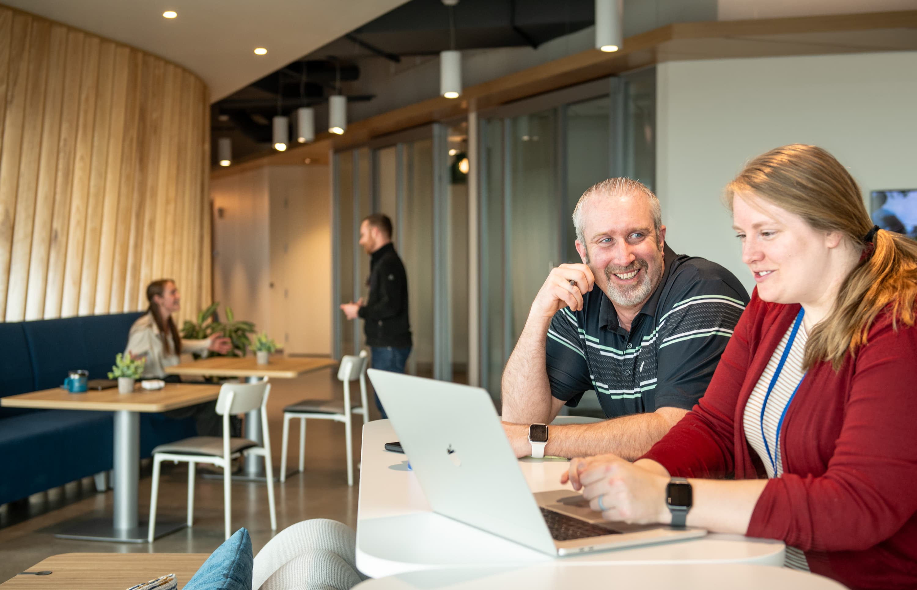 An adult woman sits at a computer next to an adult man as they smile.