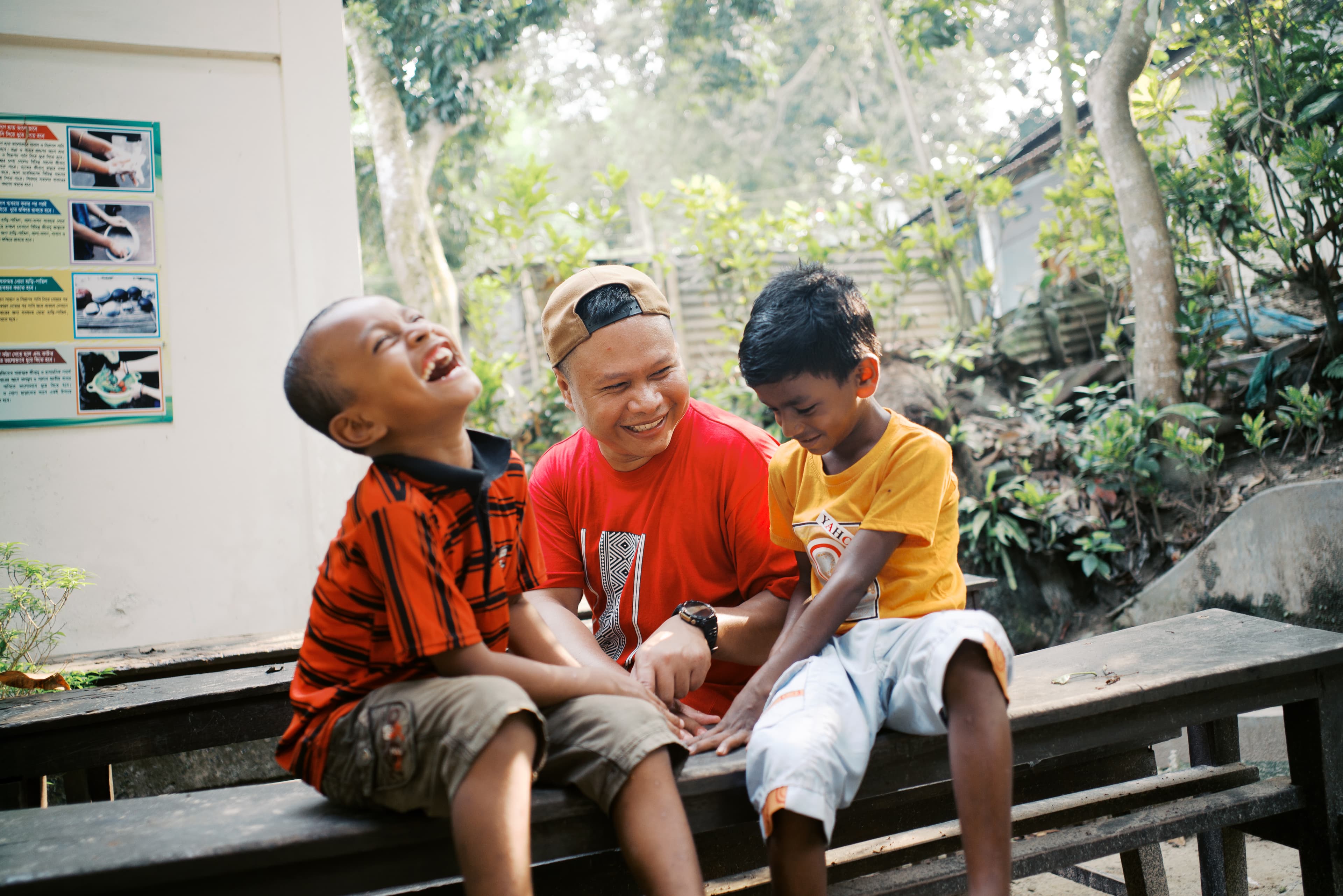 Two young boys giggle while sitting on a wooden bench with an older man as they play a game.