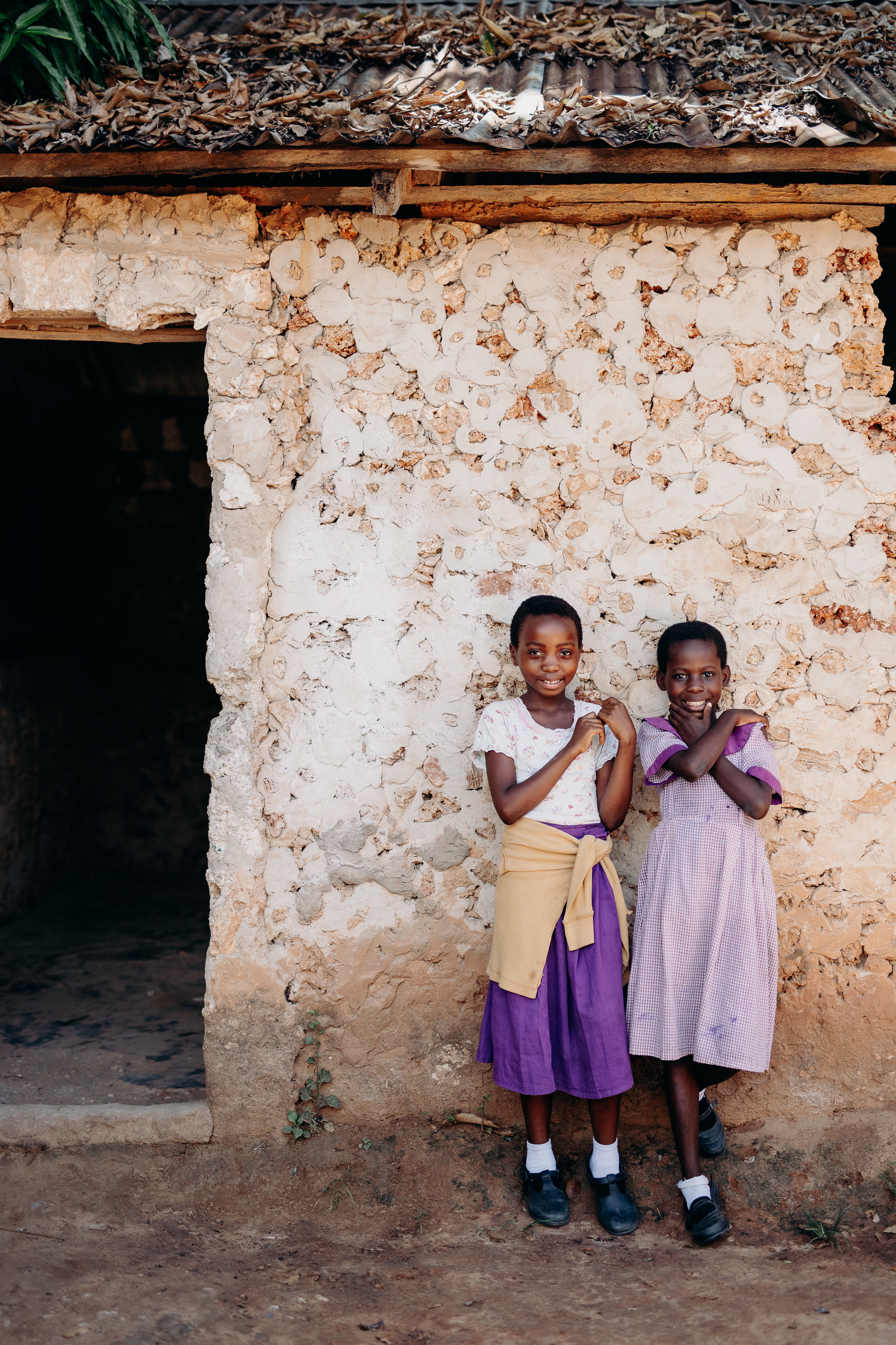 Two young girls are standing against a brick wall outside their school.