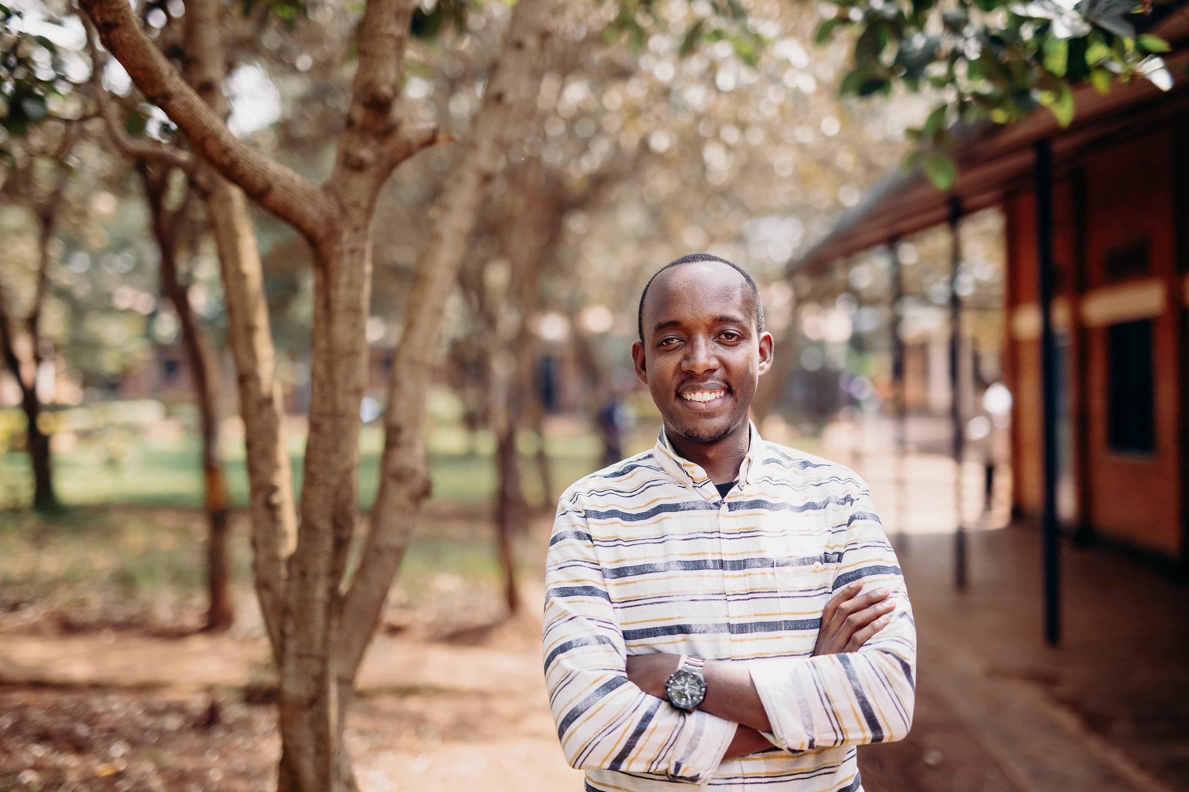 A young man wearing a striped shirt stands with his arms crossed and smiles for the camera.