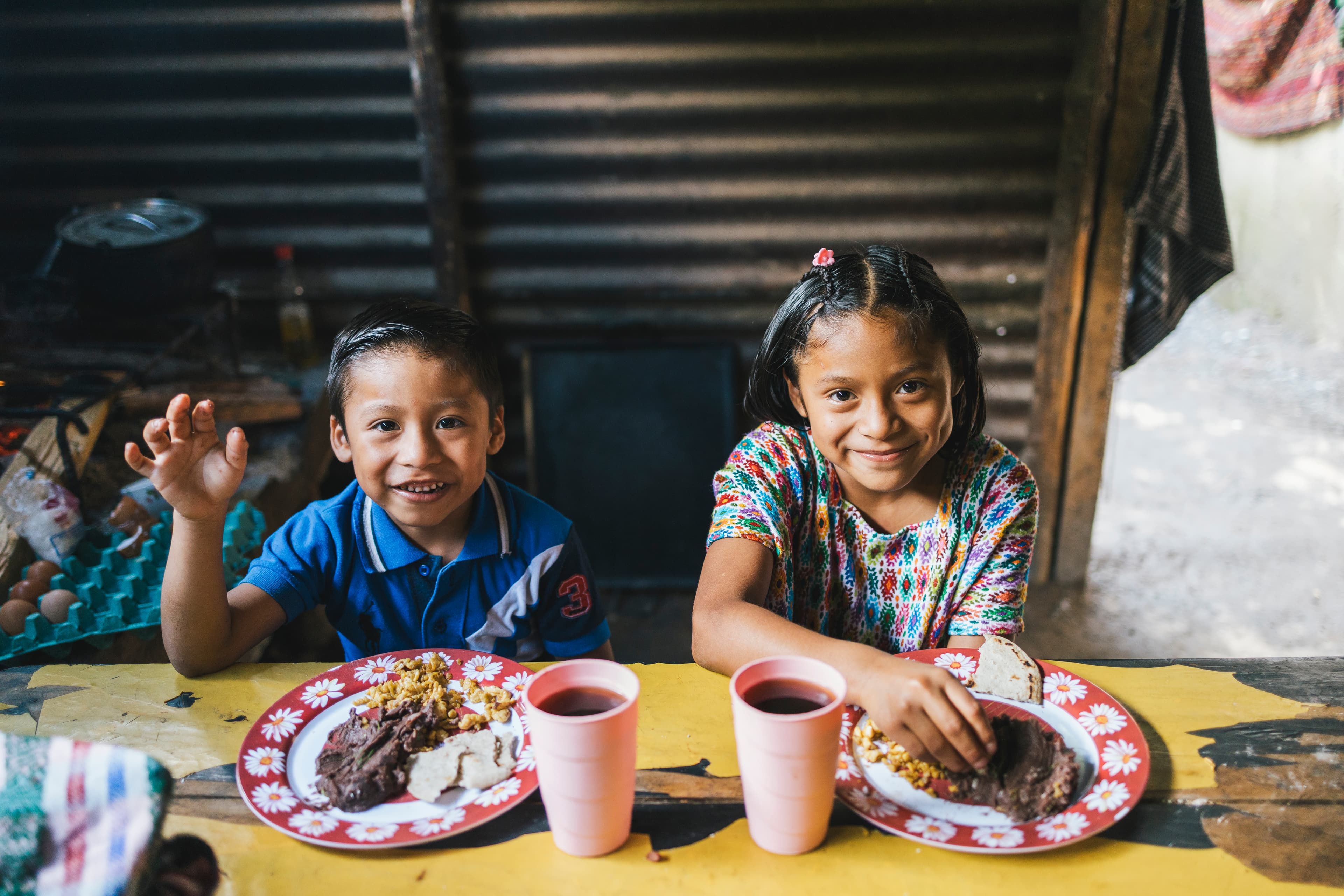 A young boy and girl are sitting at a table smiling and eating breakfast together.