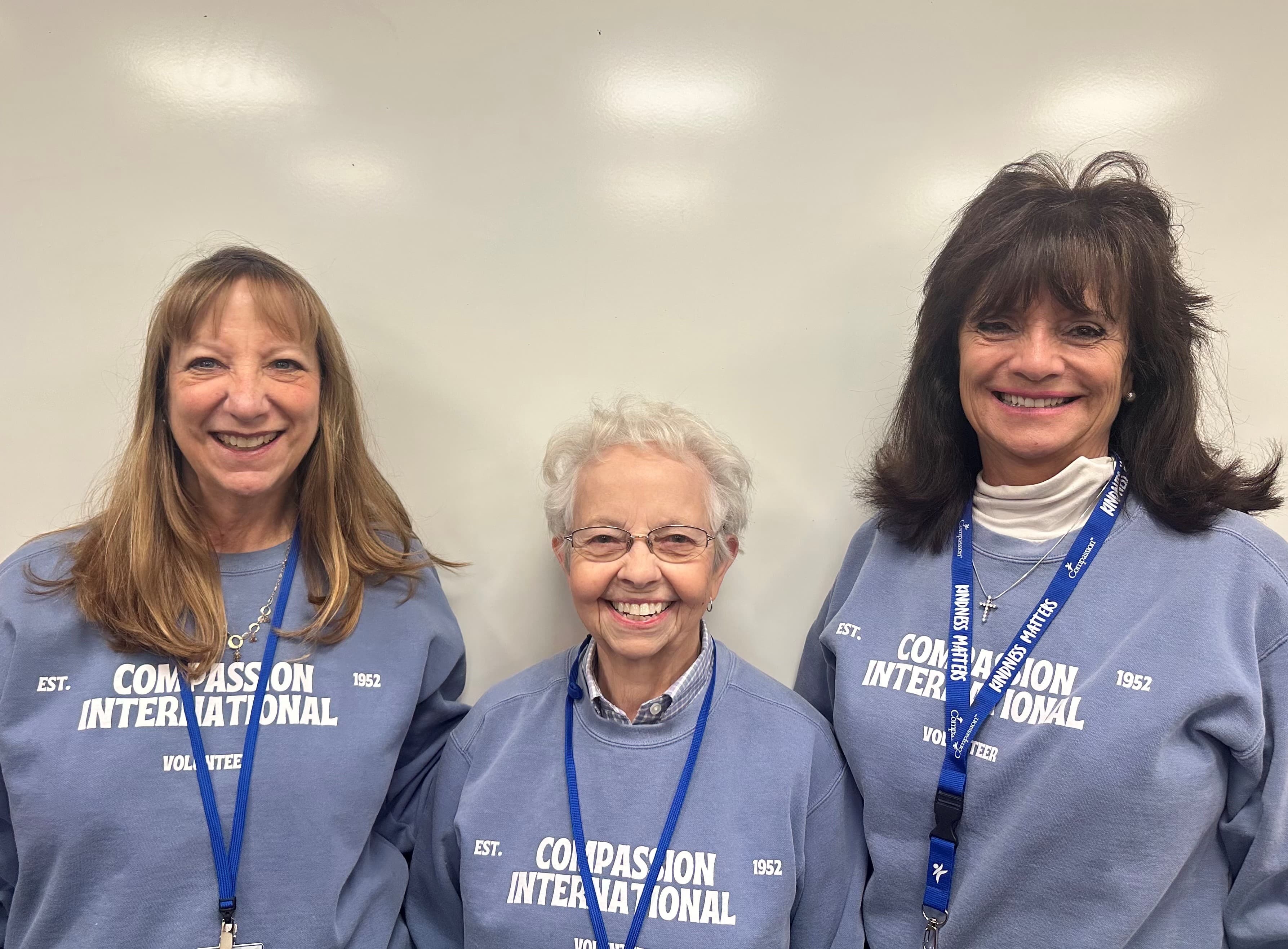 Three women are standing together wearing volunteer sweatshirts.