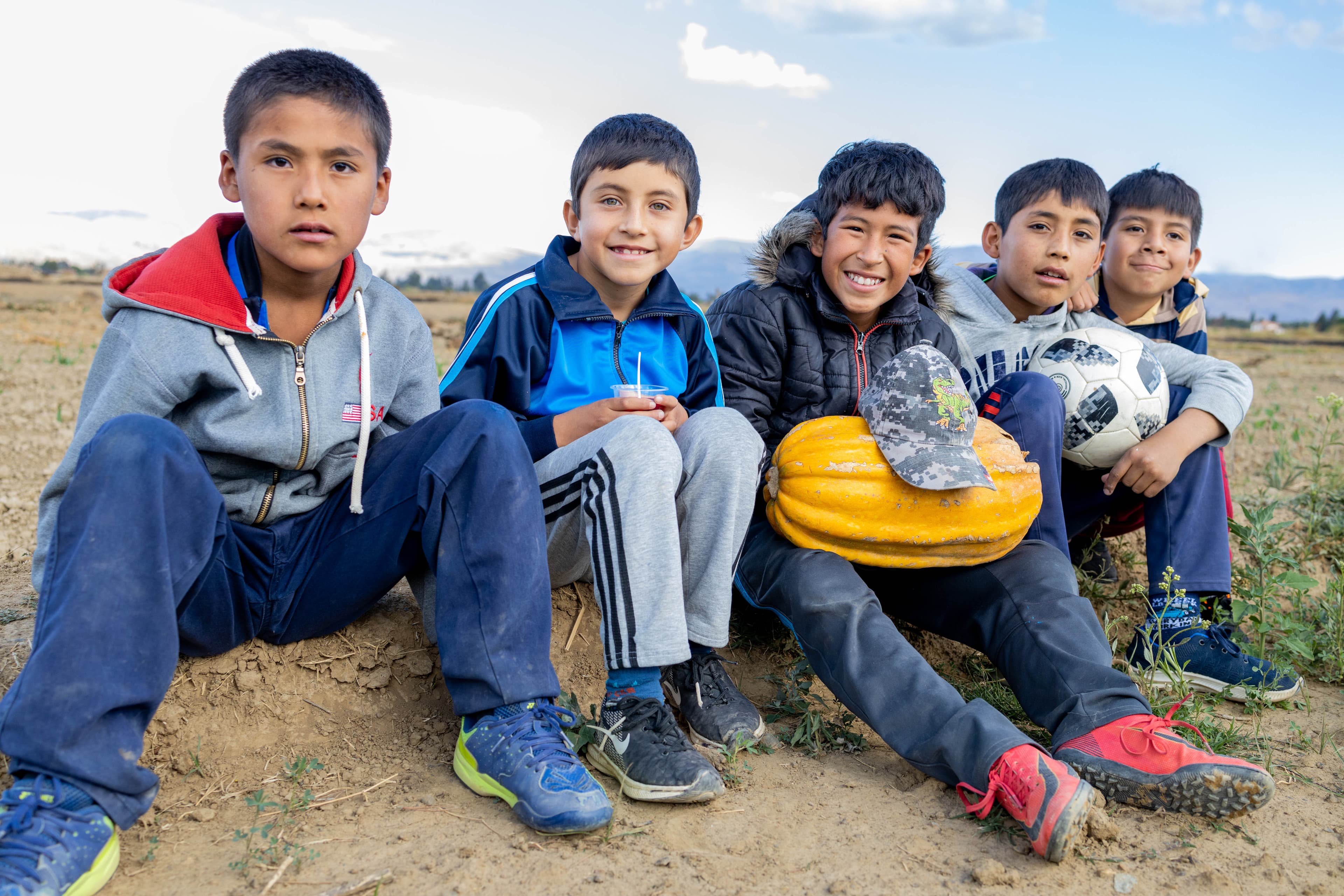 A group of young boys are sitting and smiling, holding a soccer ball.