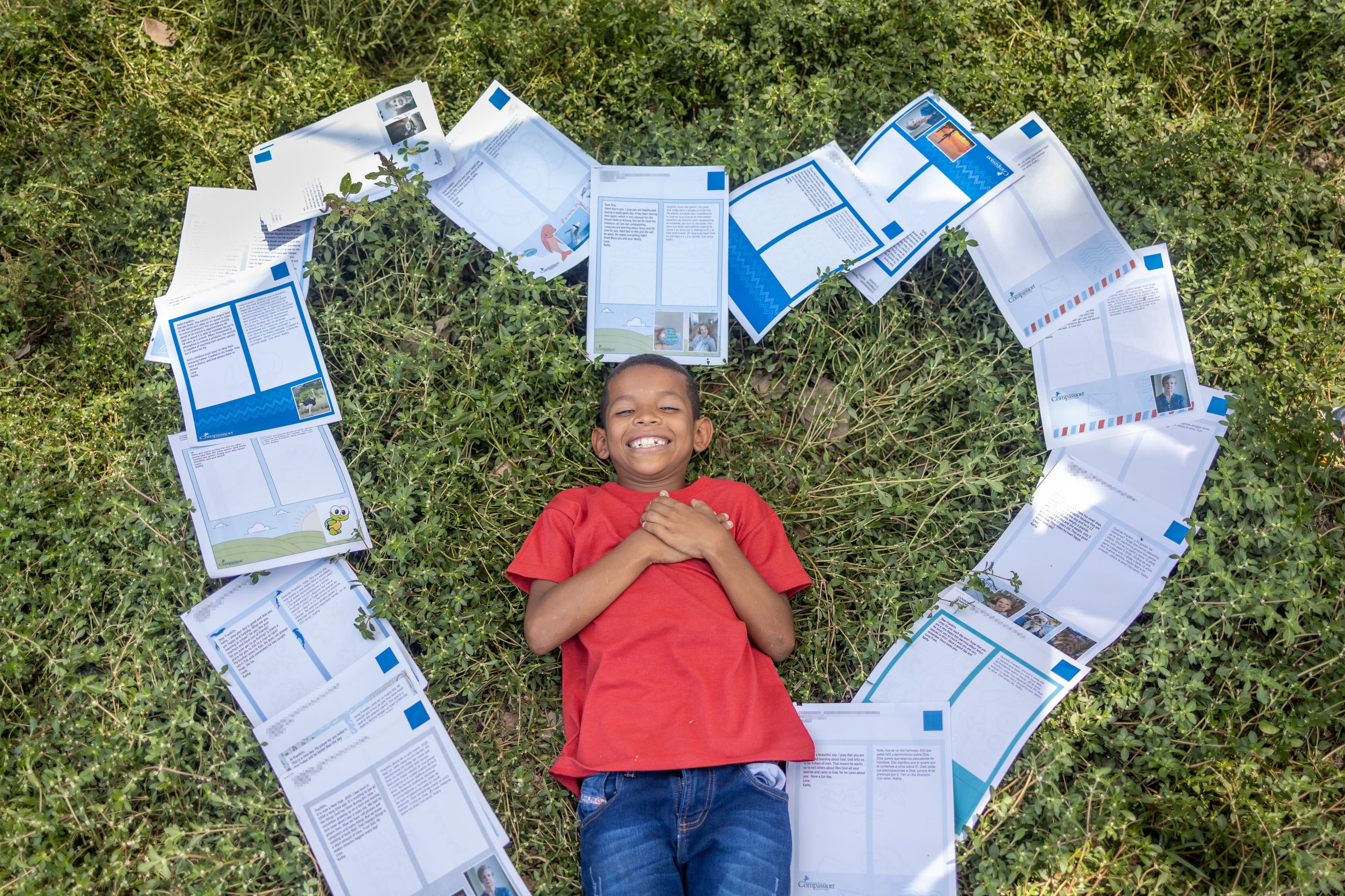Boy lies on the ground, smiling with his hands over his heart. Papers in the shape of a heart surround him.