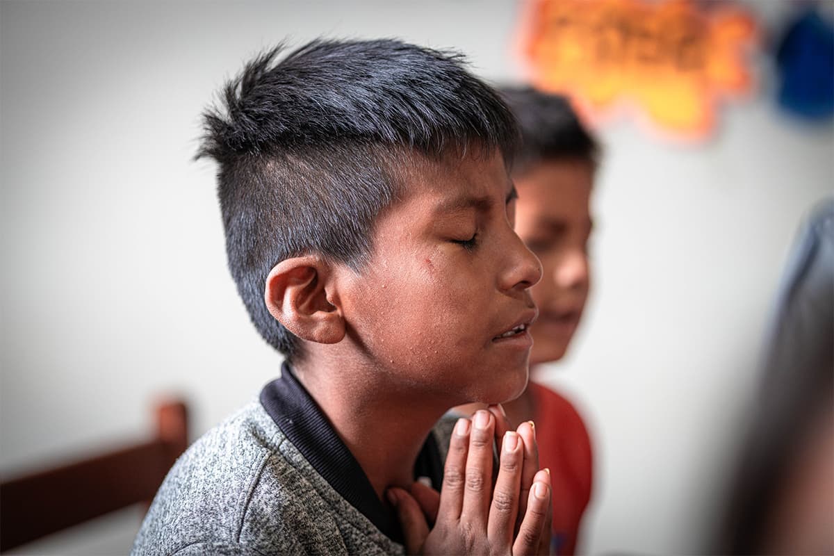 A young boy is praying with his eyes closed and hands held together against his face.