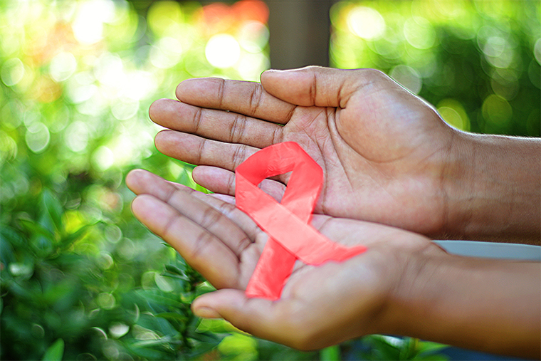 Two hands holding a red AIDS ribbon